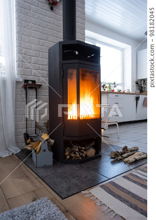 Black stove, fireplace in interior of house in loft style. Alternative eco-friendly heating, warm cozy room at home, burning wood Black stove, fireplace in interior of house in loft style. Alternative eco-friendly heating, warm cozy room at home, burning wood 98182045