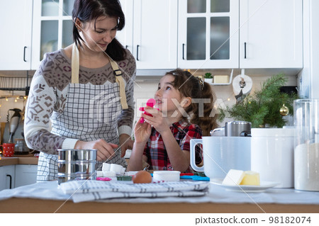 Mom and daughter in the white kitchen are preparing cookies for Christmas and new year. Family day, preparation for the holiday, learn to cook delicious pastries, cut shapes out of dough with molds 98182074