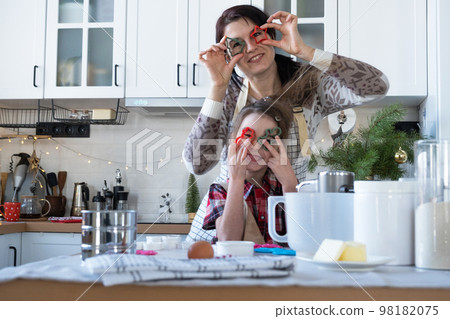 Mom and daughter in the white kitchen are preparing cookies for Christmas and new year. Family day, preparation for the holiday, learn to cook delicious pastries, cut shapes out of dough with molds 98182075