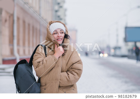 A cute girl in a coat and hat walks around the city in bad cold weather, hiding from the wind A cute girl in a coat and hat walks around the city in bad cold weather, hiding from the wind 98182679