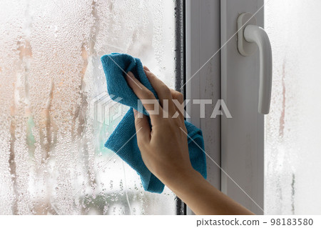 A womans hand wipes the condensate from the window glass with a towel. 98183580