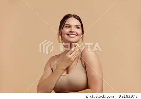 Face massage. Plus Size Woman Holding Jade Facial Roller for Skin Care 98183975