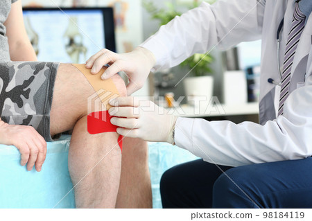 Physiotherapist applying kinesiotape to patient knee in clinic closeup Physiotherapist applying kinesiotape to patient knee in clinic closeup 98184119