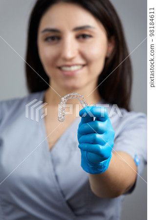 Dentist holdind orthodontic transparent silicone trainer or aligner for teeth correction 98184611