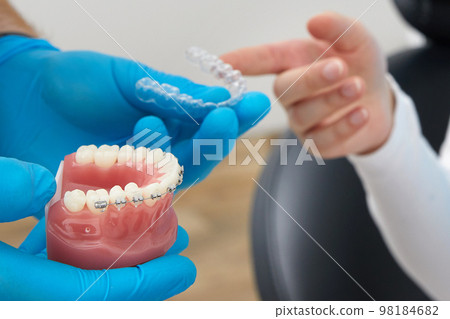 Orthodontist showing model of human jaw with wire braces and aligners explaining the difference 98184682