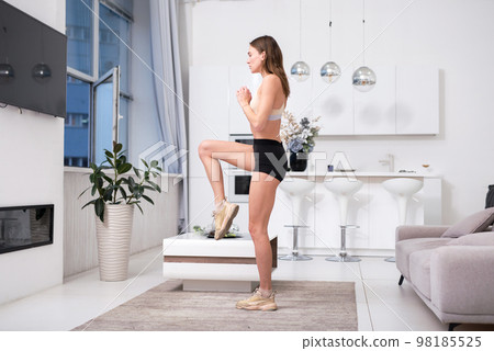 Fit woman exercising at home, workout, raises her knees high, steps in place Fit woman exercising at home, workout, raises her knees high, steps in place 98185525