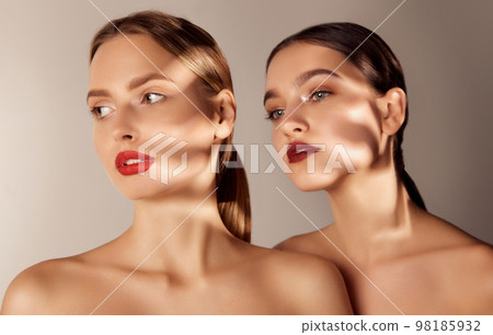 Portrait of two young, beautiful blonde and brunette girls with red lips makeup isolated over grey studio background. Shadows. Concept of skincare, cosmetology, natural beauty 98185932