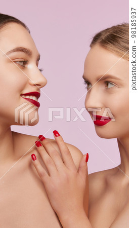 Portrait of two young, beautiful girls with well-kept skin and red lips makeup isolated over pink studio background. Concept of skincare, cosmetology, natural beauty Portrait of two young, beautiful girls with well-kept skin and red lips makeup isolated over pink studio background. Concept of skincare, cosmetology, natural beauty 98185937