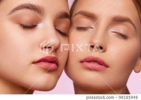 Tender naturality. Portrait of two young, beautiful girls with well-kept skin isolated over pink studio background. Concept of skincare, cosmetology, natural beauty 98185949