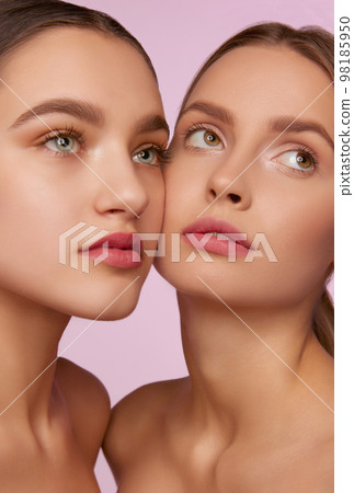 Clear smooth skin. Portrait of two young, beautiful girls with well-kept skin isolated over pink studio background. Concept of skincare, cosmetology, natural beauty 98185950