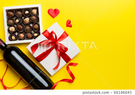 Bottle of red wine on colored background for Valentine Day with gift and chocolate. Heart shaped with gift box of chocolates top view with copy space Bottle of red wine on colored background for Valentine Day with gift and chocolate. Heart shaped with gift box of chocolates top view with copy space 98186845