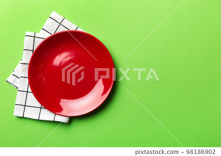 Top view on colored background empty round red plate on tablecloth for food. Empty dish on napkin with space for your design Top view on colored background empty round red plate on tablecloth for food. Empty dish on napkin with space for your design 98186902
