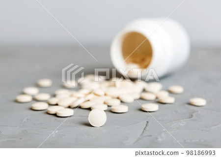 Medicine bottle and white pills spilled on a light background. Medicines and prescription pills flat lay background. White medical pills and tablets spilling out of a drug bottle 98186993
