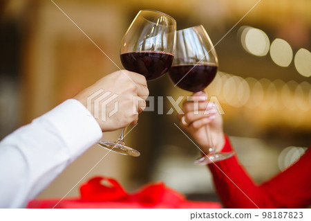 Couple clink glasses with red wine. Lovers give each other gifts. Lovely romantic dinner. 98187823