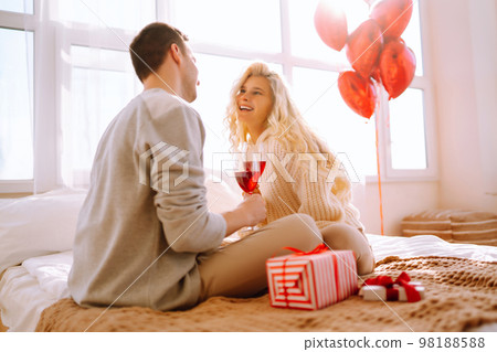 Beautiful young couple at home celebrating Valentine's Day. Lovers give each other gifts. Beautiful young couple at home celebrating Valentine's Day. Lovers give each other gifts. 98188588