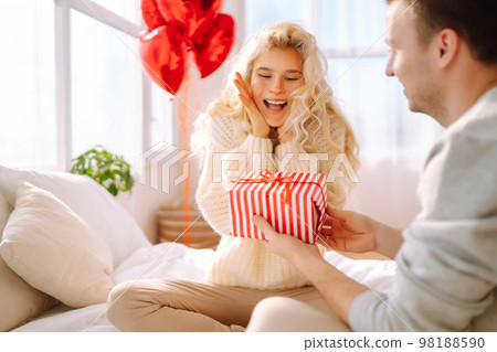 Beautiful young couple at home celebrating Valentine's Day. Lovers give each other gifts. Beautiful young couple at home celebrating Valentine's Day. Lovers give each other gifts. 98188590