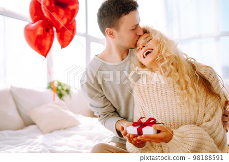Beautiful young couple at home celebrating Valentine's Day. Lovers give each other gifts. Beautiful young couple at home celebrating Valentine's Day. Lovers give each other gifts. 98188591
