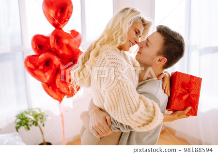 Beautiful young couple at home celebrating Valentine's Day. Lovers give each other gifts. Beautiful young couple at home celebrating Valentine's Day. Lovers give each other gifts. 98188594