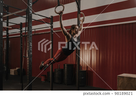 Young crossfit woman swinging on gymnastic rings. 98189021