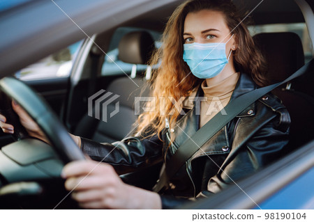 Young woman driving a car wearing on a medical mask during an epidemic. Transport isolation. Covid. 98190104