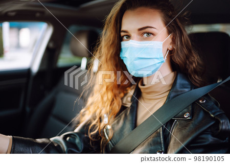 Young woman driving a car wearing on a medical mask during an epidemic. Transport isolation. Covid. Young woman driving a car wearing on a medical mask during an epidemic. Transport isolation. Covid. 98190105