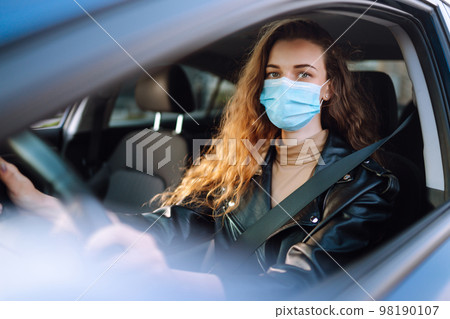 Young woman driving a car wearing on a medical mask during an epidemic. Transport isolation. Covid. Young woman driving a car wearing on a medical mask during an epidemic. Transport isolation. Covid. 98190107
