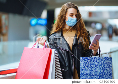 Fashionable woman in protective medical mask with multi-colored bags in modern shop center. Fashionable woman in protective medical mask with multi-colored bags in modern shop center. 98190109