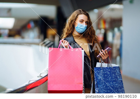 Fashionable woman in protective medical mask with multi-colored bags in modern shop center. Fashionable woman in protective medical mask with multi-colored bags in modern shop center. 98190110