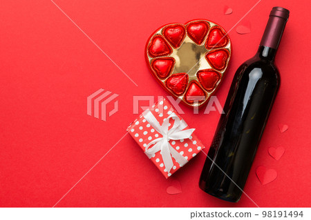 Bottle of red wine on colored background for Valentine Day with gift and chocolate. Heart shaped with gift box of chocolates top view with copy space Bottle of red wine on colored background for Valentine Day with gift and chocolate. Heart shaped with gift box of chocolates top view with copy space 98191494