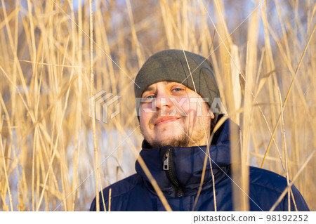 Cheerful happy young male man on high dry reeds. European caucasian white smiling man portrait, positive emotion. Winter hiking, leisure activities. Cheerful happy young male man on high dry reeds. European caucasian white smiling man portrait, positive emotion. Winter hiking, leisure activities. 98192252