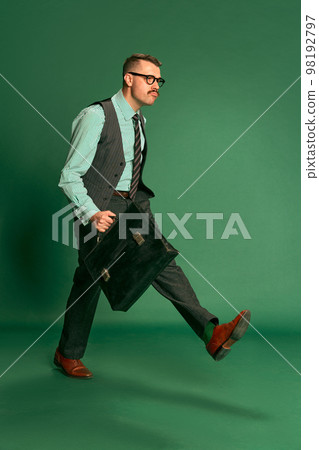 Portrait of handsome man, businessman in classical suit with briefcase walking to work over green studio background. Concept of emotions, occupation, lifestyle 98192797