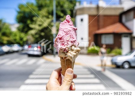 Ice cream in hand. Waffle cone with ice cream on the background of the street in the summer on a hot day. Street food, sweets, desserts concept. 98193982