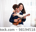 Young Asian lesbian couple intending to play a musical instrument together, guitar and kalimba, in the living room at home, the lifestyle of couple LGBT loving women happy in romantic love and fun 98194518