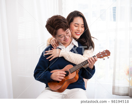 Young Asian lesbian couple intending to play a musical instrument together, guitar and kalimba, in the living room at home, the lifestyle of couple LGBT loving women happy in romantic love and fun Young Asian lesbian couple intending to play a musical instrument together, guitar and kalimba, in the living room at home, the lifestyle of couple LGBT loving women happy in romantic love and fun 98194518