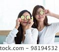 Home spa. Two beautiful young women place pieces of cucumber on their cheek in the home spa.. 98194532