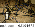 Electrical plugs with cords connected to power strip. Cable power cords in a tangled mess on floor of workplace, used dirty electric outlet 98194672