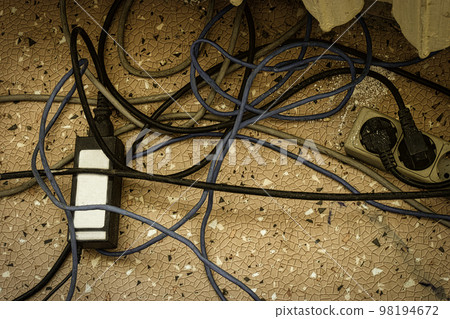 Electrical plugs with cords connected to power strip. Cable power cords in a tangled mess on floor of workplace, used dirty electric outlet 98194672