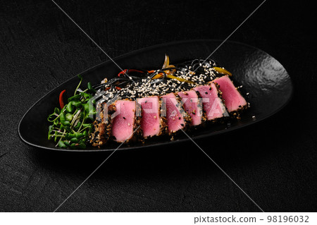 Baked tuna served with black noodles on black background 98196032