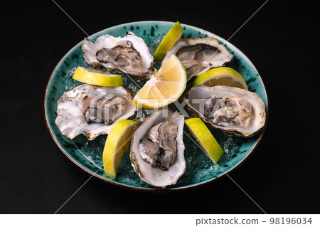 Oysters served with lemon and ice on blue plate on black background 98196034