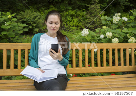 Outdoor portrait of a college student with a phone and a book Outdoor portrait of a college student with a phone and a book 98197507