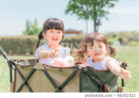 Sister girls (children, toddlers, girls) playing on a carry cart in the park 98202322