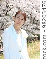A woman in her 40s standing in an entrance ceremony outfit with cherry blossoms in the background, upper body 98203476