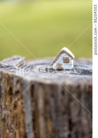 A cute rustic little house made of unglazed pottery on top of a log 98204503
