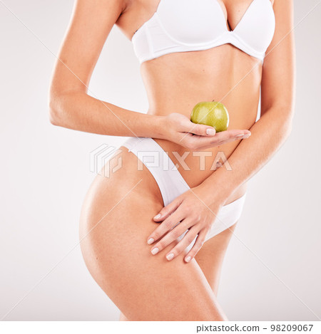 Lingerie, skincare and body of woman with apple in studio isolated on a gray background. Underwear, food and female model holding fruit for nutrition, vitamin c or healthy diet, body care or beauty. 98209067