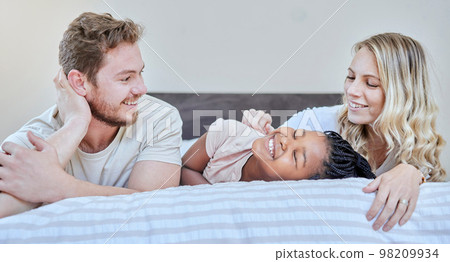 Family, adoption and love with happy, smile and care together on bed, relax and fun on weekend in home. Diversity, bedroom and happiness with bonding, support and relaxing with moth, father and girl 98209934