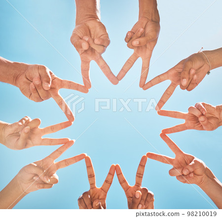 Teamwork, community and group support with fingers in a star shape from below against a blue sky background. A diverse crowd of people with hands joined together for motivation, unity and peace 98210019