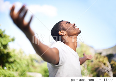 Under the wide blue sky. a young man with arms outstretched outdoors. Under the wide blue sky. a young man with arms outstretched outdoors. 98211828