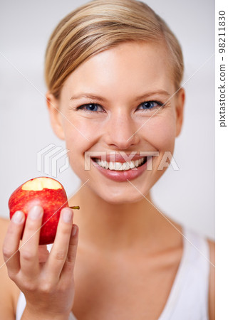 Fresh and healthy is the way to go. A portrait of a beautiful young woman eating a delicious red apple. 98211830