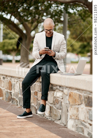 Stylish, cool smiling businessman on a phone in the park outside in nature. Happy man texting, chatting or reading social media messages on a smartphone outdoors on a break from work with copy space 98211895
