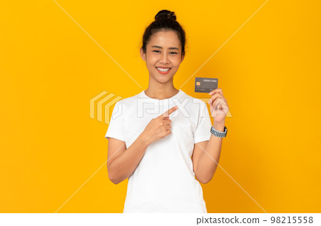 Cheerful beautiful Asian woman holding mockup credit card on orange background. Cheerful beautiful Asian woman holding mockup credit card on orange background. 98215558